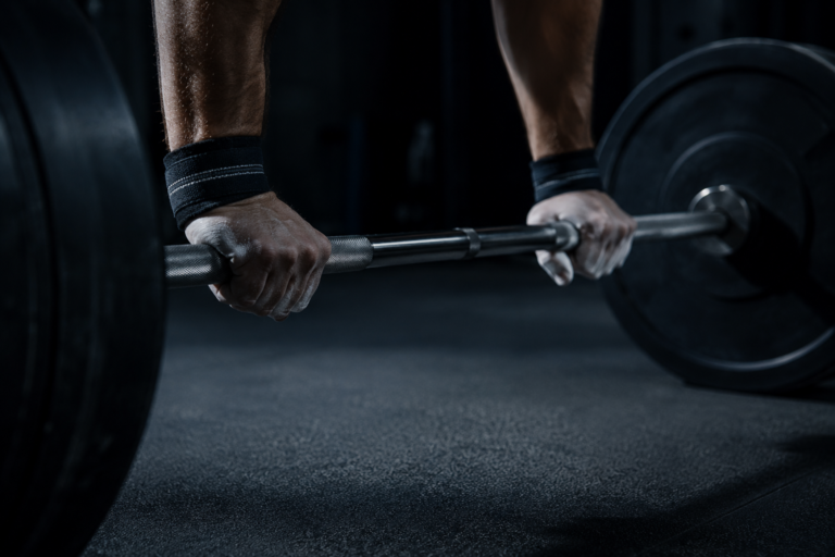 Man's hands gripping a barbell in a gym, dramatic side lighting, representing disciplined training on GLP-1